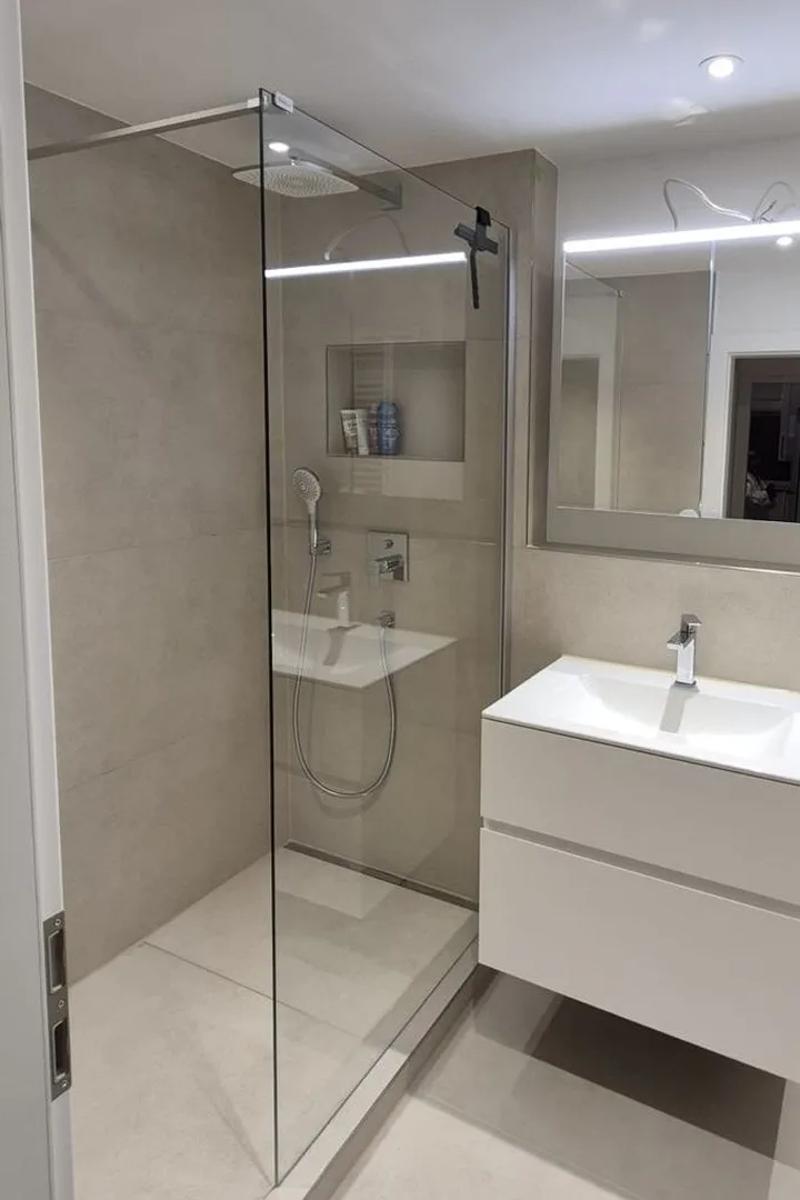 Badezimmer nach der Sanierung: bodengleiche Dusche mit Glaswand, beige Großformatfliesen