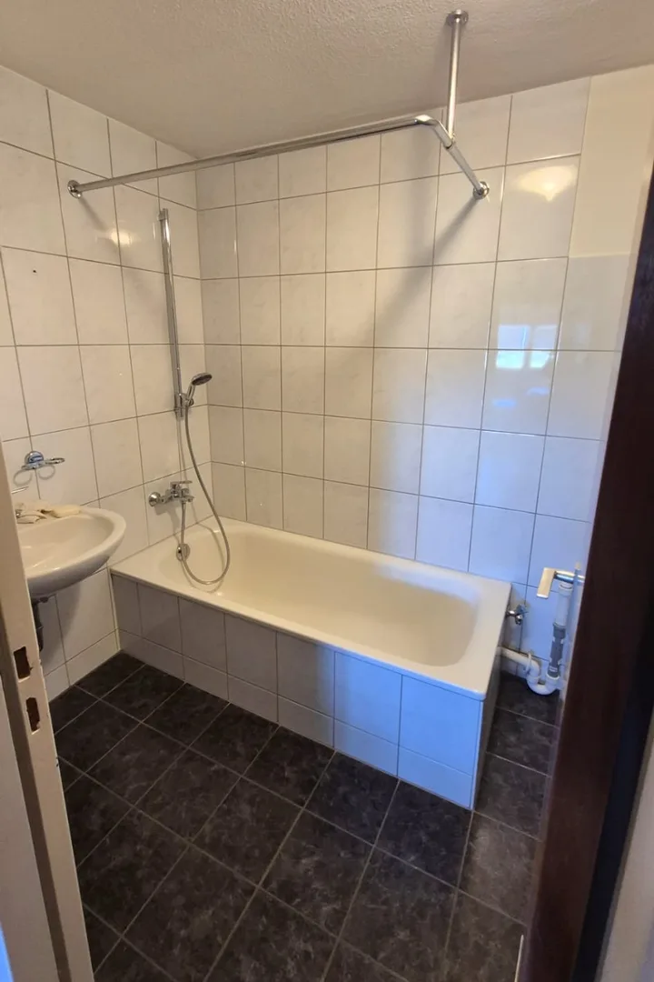 Badezimmer vor der Sanierung: weiße Wandfliesen, Badewanne, dunkler Boden